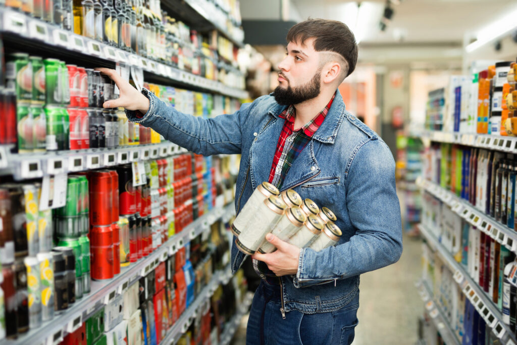 Interested young man making purchases in grocery store, buying canned beer